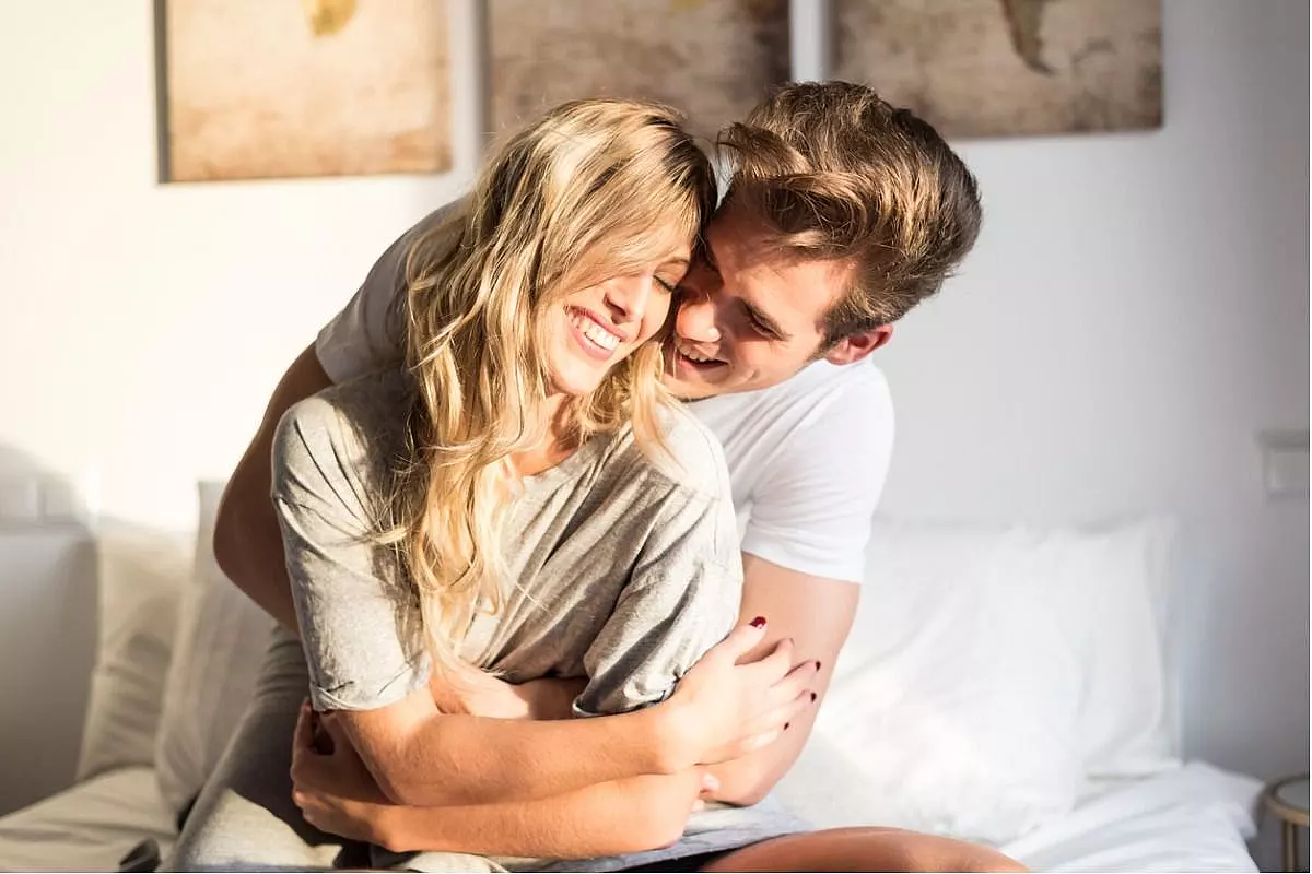 Giovane coppia felice (uomo e donna) rilassata sul letto mentre si abbraccia