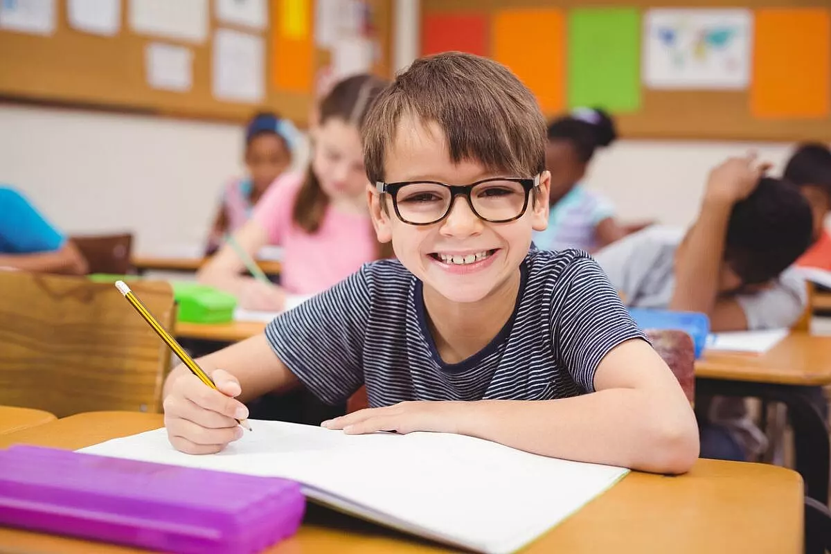 Bambino in classe con gli occhiali che fa i compiti