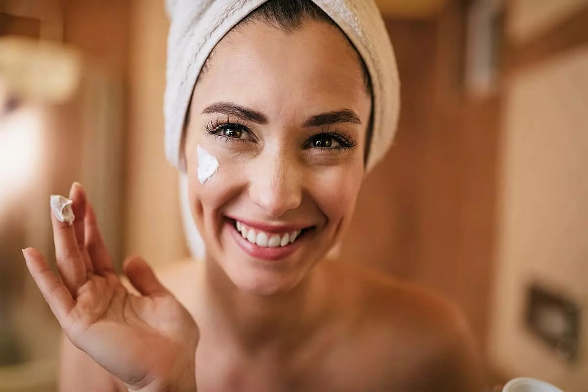 Donna sorridente con un turbante applica una crema viso nutriente