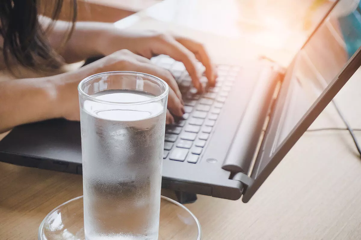 Donna con bicchiere di acqua mentre lavora al computer